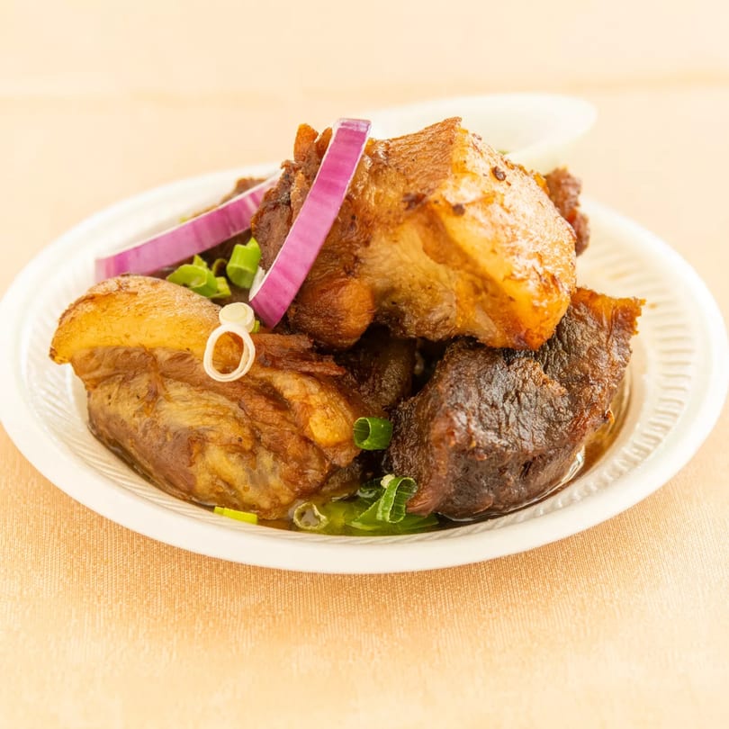 Braised pork belly pieces garnished with red onion and green onion on a white plate.