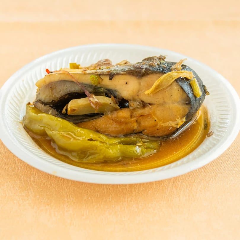 Fish steak with green peppers in a savory sauce on a white plate.