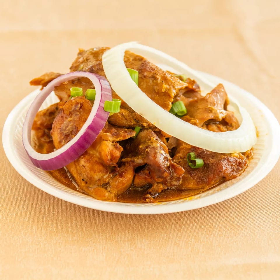 Stewed meat in brown sauce, garnished with white and red onion rings, and green onions on a white plate.