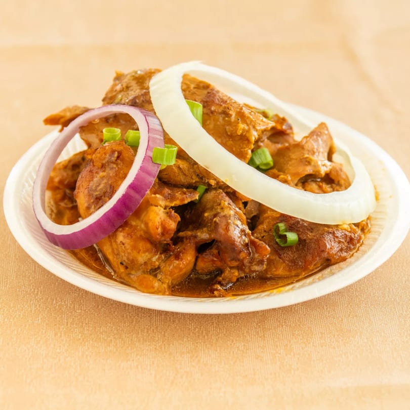 Stewed meat in brown sauce, garnished with white and red onion rings, and green onions on a white plate.