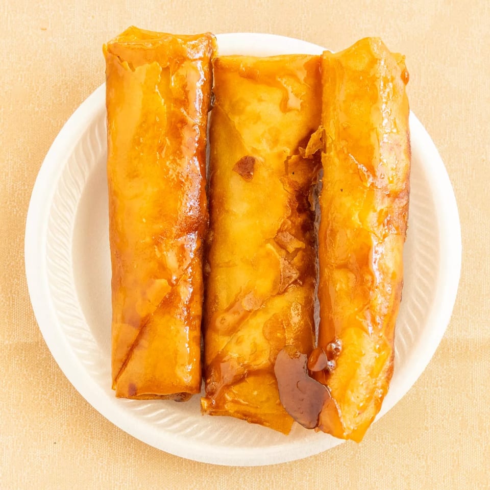 Three golden-brown glazed rolls on a white plate, presented on a light tan surface.