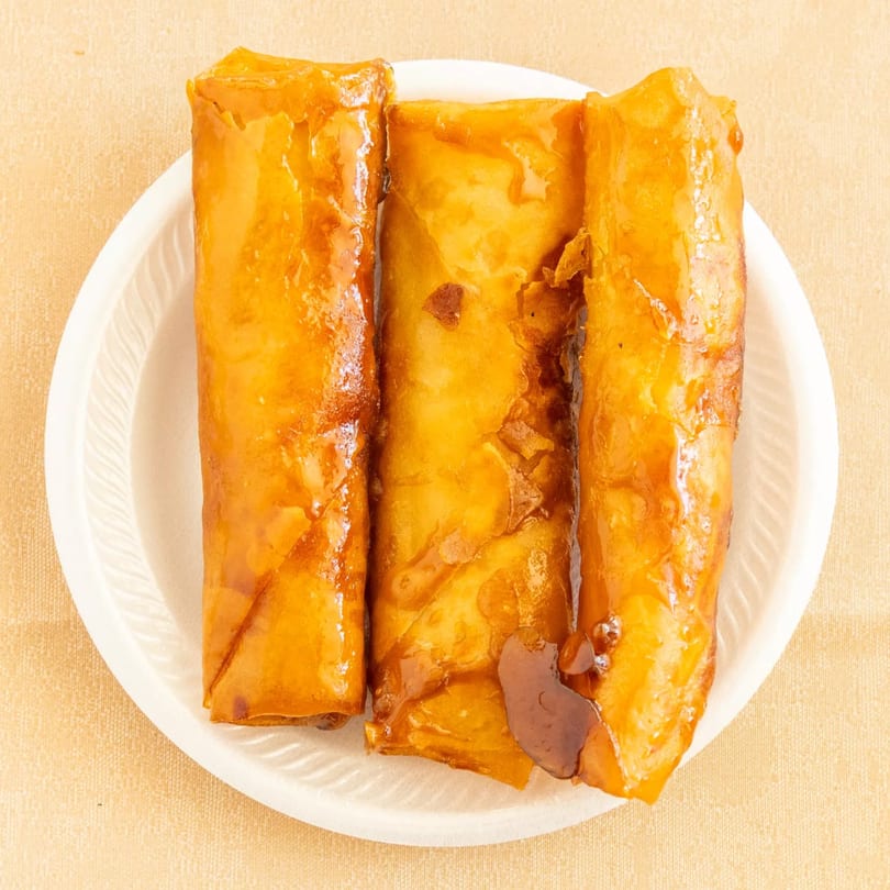 Three golden-brown glazed rolls on a white plate, presented on a light tan surface.