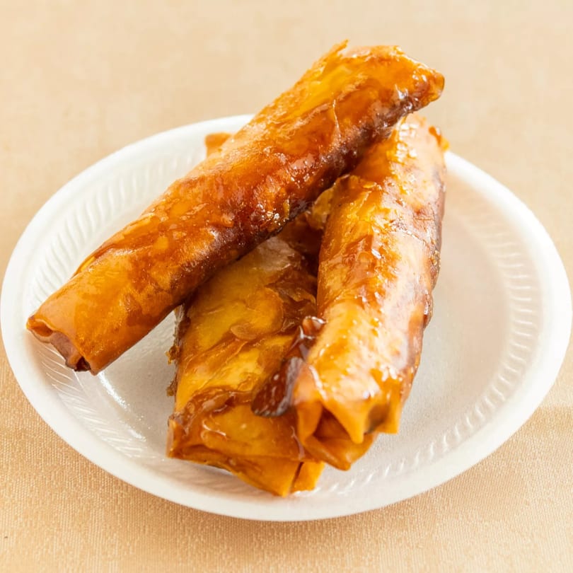 Three caramelized banana spring rolls on a white disposable plate.