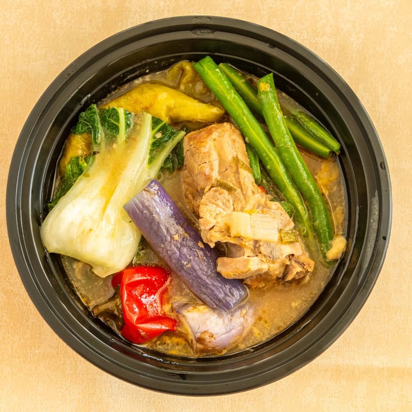 Pork ribs stew with green beans, bok choy, eggplant, and red bell pepper in a black bowl.