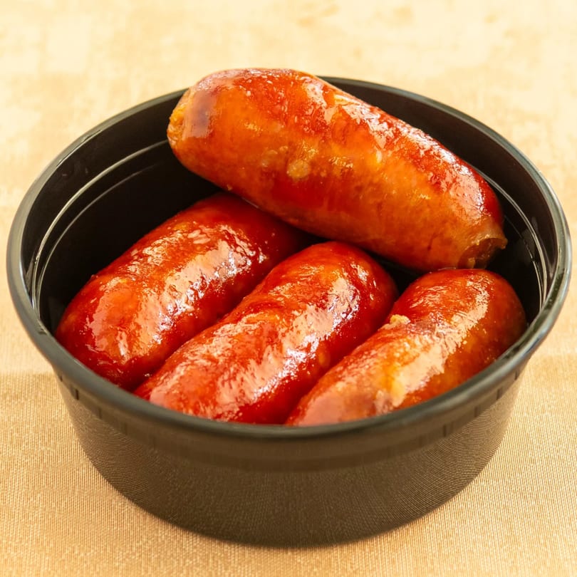Glazed sausages in a black takeout container, ready to eat.